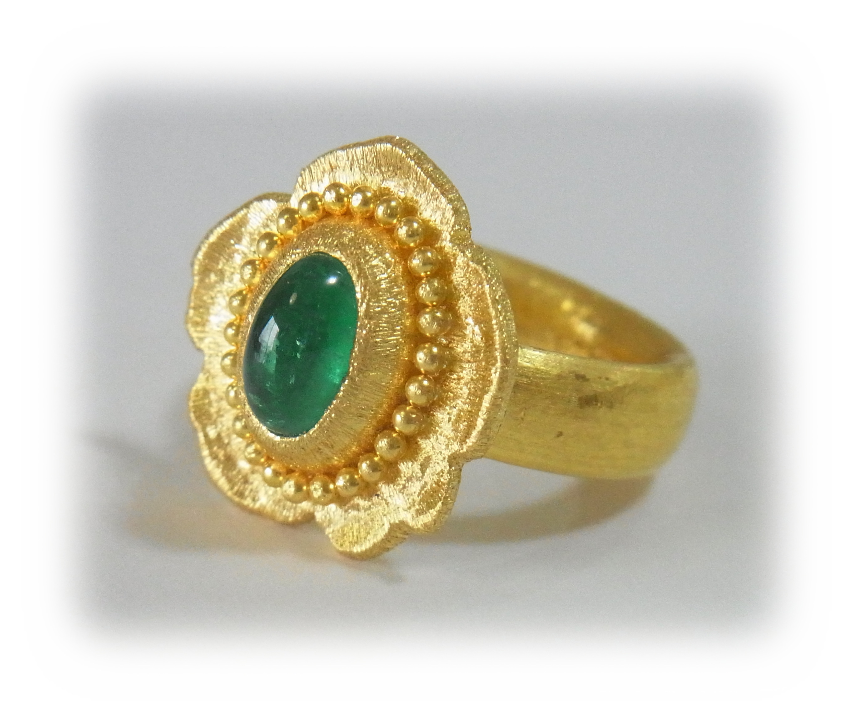 Gold ring with a cabochon-cut emerald; granulation decoration on the bezel rim (angled view)