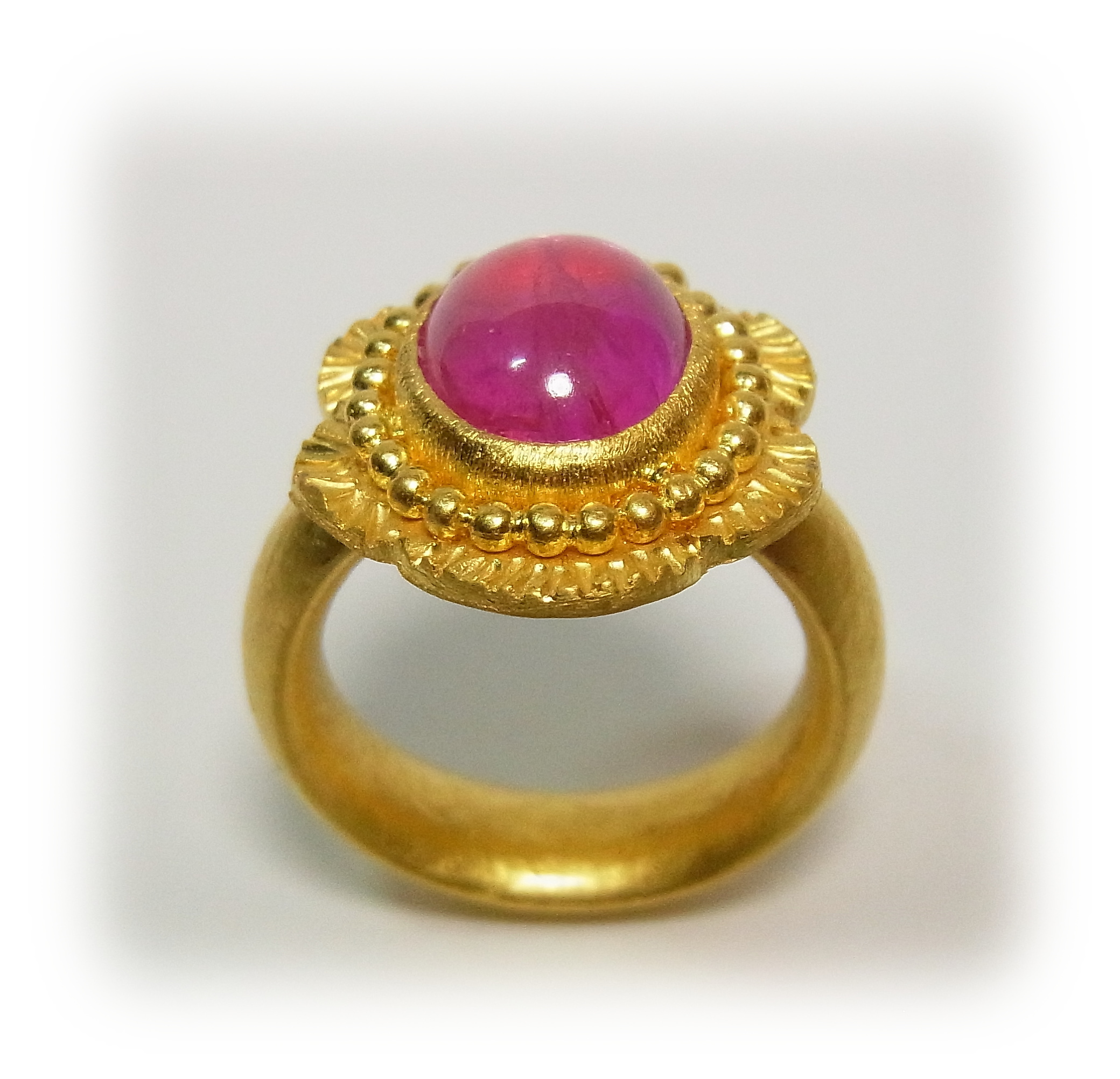 Gold ring with a cabochon-cut pink sapphire, featuring granulation decoration along the bezel's edge.