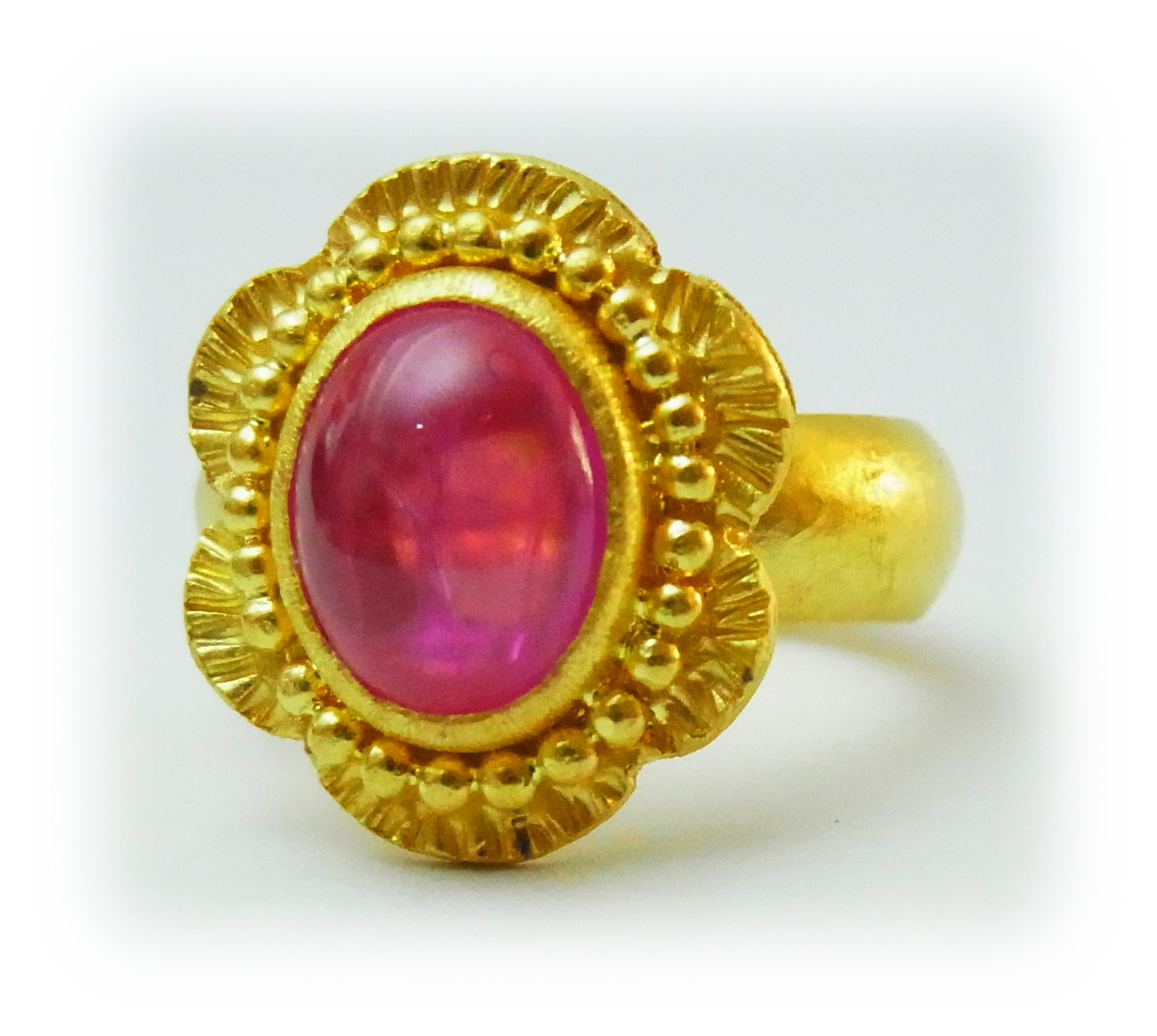 Gold ring with a cabochon-cut pink sapphire, featuring granulation decoration along the bezel's edge.