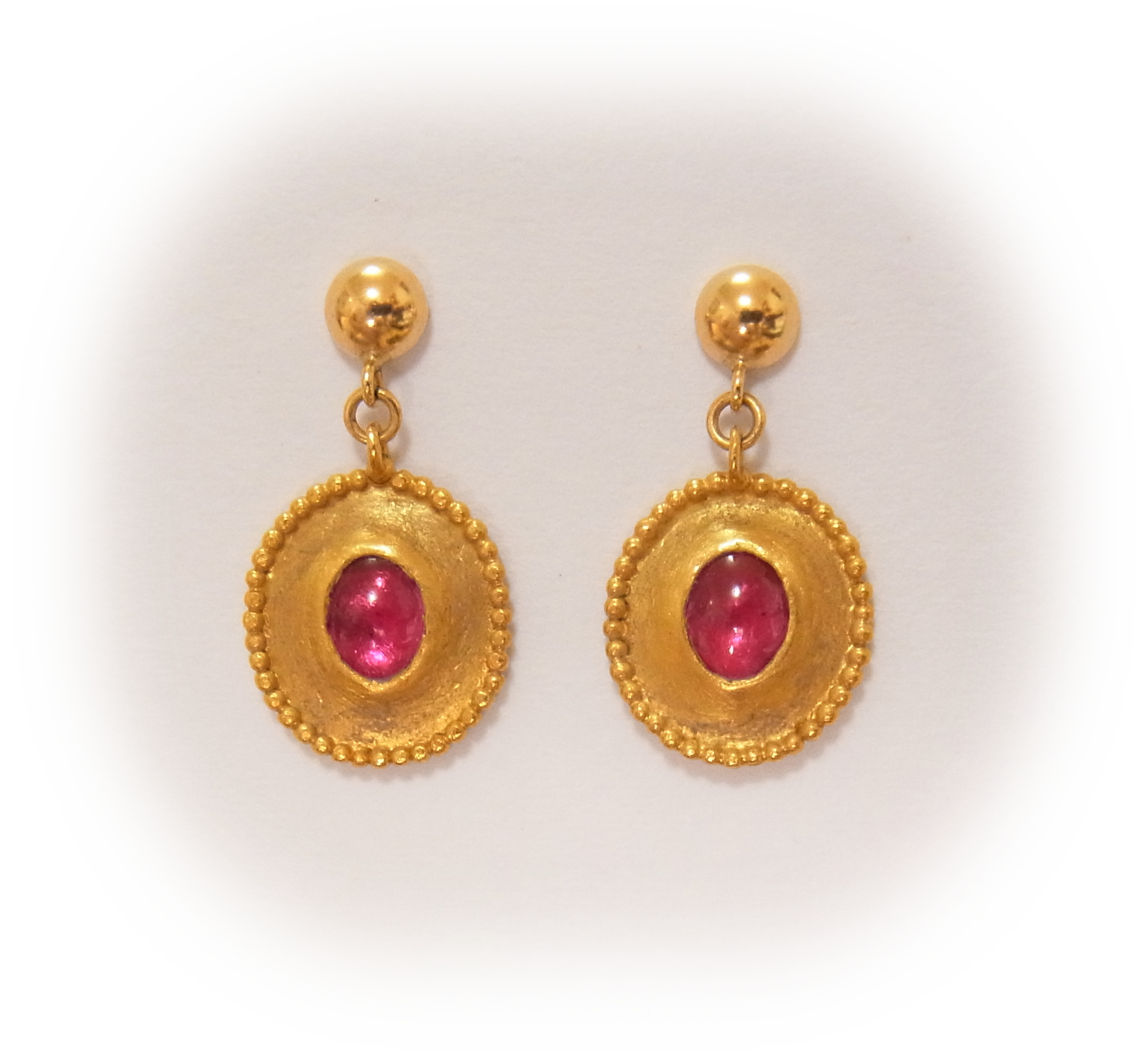 Gold earrings set with cabochon rubies, featuring granulation decoration along the oval rims.